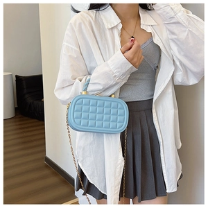 Detail of light blue mini box bag with gold chain strap and quilted texture on light fabric