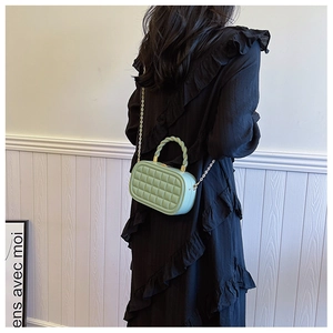 Detail of mint green quilted bag with woven handle and gold chain on black dress