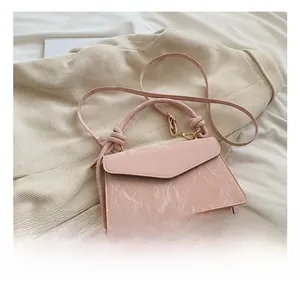Détail du mini sac en cuir verni rose clair texturé avec poignée et bandoulière fine