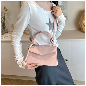 Detailed close-up of a pink pleated square bag worn crossbody with a knotted handle