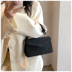 Close-up of black pleated leather handbag with gold hardware on a minimalist suit