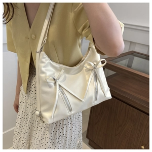 Detail of cream shoulder bag featuring elegant bow accents and silver zipper hardware