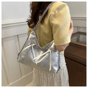 Detail of silver metallic leather tote bag with bow ribbon and zipper accents on a model