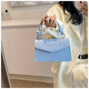 Détail d'un sac à main bleu clair texturé avec poignée nouée et anneaux dorés