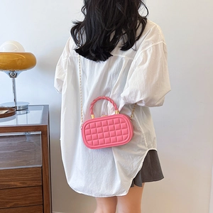 Pink woven texture mini box bag with gold chain strap shown on person in a warm room