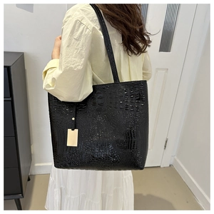 Detail of black crocodile embossed tote bag with gold metal plate on a shoulder strap