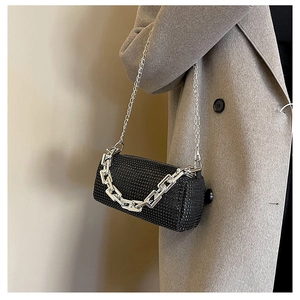 Detail of black rhinestone cylinder bag with thick silver chain on grey coat