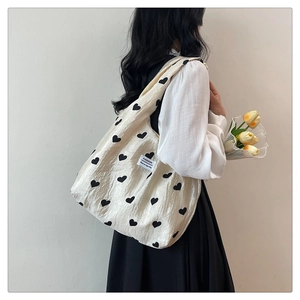 Detail of beige canvas tote bag featuring black heart prints and soft pleated texture