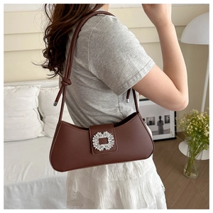 Detail of a brown shoulder bag with a sparkling square rhinestone buckle on leather