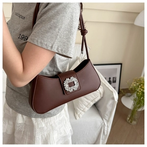 Close-up of a brown underarm bag with a sparkling crystal square buckle and leather strap