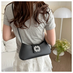 Détail d'un sac sous les bras en cuir noir avec une boucle en strass sur l'épaule