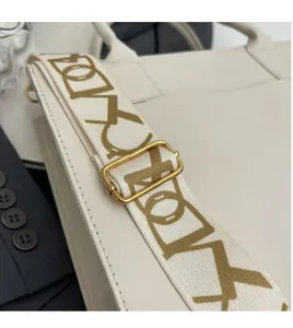 Détail de la large bandoulière crème avec motifs géométriques et boucles dorées chic