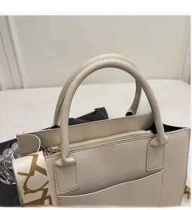 Détail de la bandoulière large et de la poignée sur un sac cabas beige orné de motifs dorés