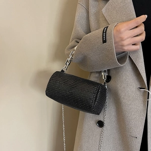 Fashionable black rhinestone cylinder bag with silver chain strap shown on model coat