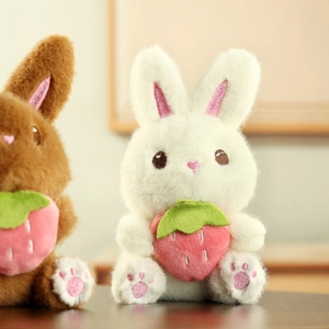 Gros plan de lapins en peluche blancs et marrons tenant des fraises au pelage doux