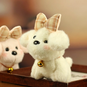 Close-up of white plush puppy keychain with plaid bow and gold bell in a wooden tray