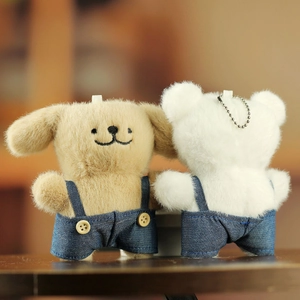 Détail de porte-clés chien en peluche portant des salopettes en jean bleu à boutons