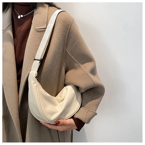 Close-up of cream canvas crescent bag with wide adjustable strap on a stylish model