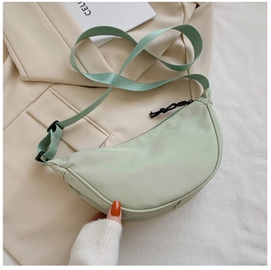 Detail of mint green half-moon crossbody bag placed on stylish beige suit and fabric