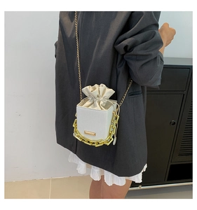 Detail van een mini bucket bag met trekkoord in gebroken wit met gouden ketting