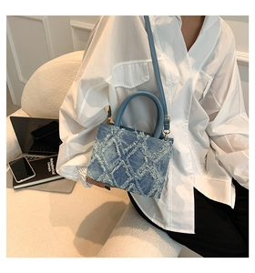 Close-up of light blue denim tote with frayed fringe diamond pattern and leather strap