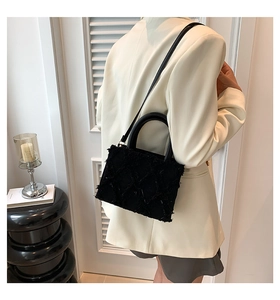 Detail of a black quilted tote bag with fringe texture shown on a model in a minimalist room