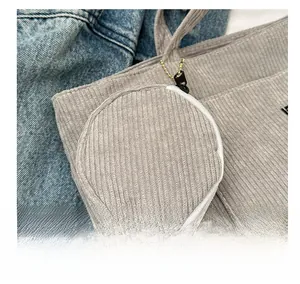 Close-up of a grey corduroy round mini pouch charm with metallic chain and zipper detail