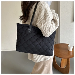 Detail shot of a black quilted tote bag with diamond stitching on a model's shoulder