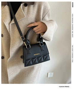 Close-up of black crossbody square bag featuring triangular quilted texture and gold hardware