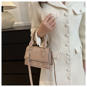 Detail of apricot quilted crossbody bag with gold buckle on white tweed jacket