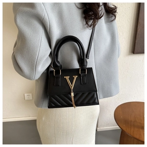 Détail du sac à main en cuir noir avec ornement en V doré et glands à franges tendance