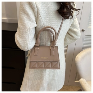 Detail of beige quilted leather handbag featuring gold hardware and a top handle