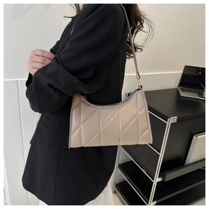 Detail view of beige quilted leather shoulder bag with diamond stitching on a black blazer