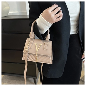 Détail d'un sac à main beige avec logo V doré, pompon et motif matelassé chic