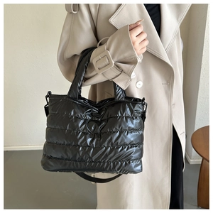 Close-up of quilted black puffer bucket bag with glossy finish and wide shoulder strap