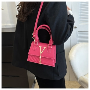 Détail du sac carré fuchsia avec logo V doré et pompon porté sur un blazer noir