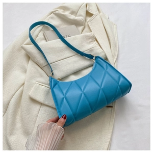 Detail of blue quilted shoulder bag with gold hardware on a beige blazer background