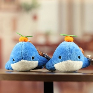 Set of two cute blue whale plush toys with small orange decorations on a wooden surface