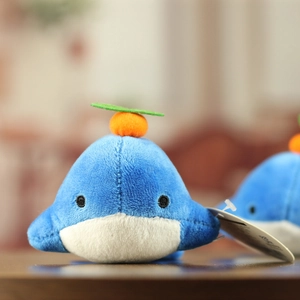 Close-up of a blue and white plush whale toy with a cute orange fruit head accessory