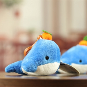 Close-up of cute blue orca plush keychain with orange fruit detail on wooden desk