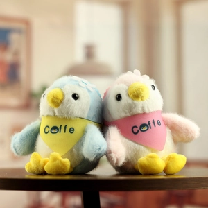Close-up of cute pink and blue plush penguins with coffee scarves on wooden surface