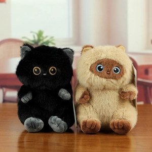 Cute plush cat keychain charms in black and beige fur with glossy eyes on wooden surface
