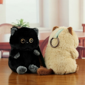 Close-up of soft plush cat keychain with fluffy fur, golden eyes, and blue satin ribbon