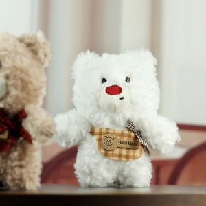 Detail of white plush teddy bear with a red nose and handmade brown checkered apron