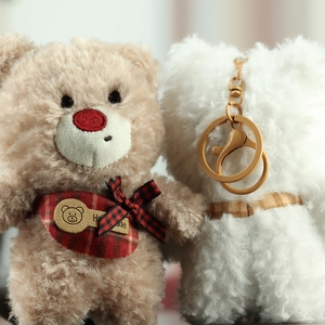 Close-up of brown and white plush teddy bear keychains with plaid bows and gold clips