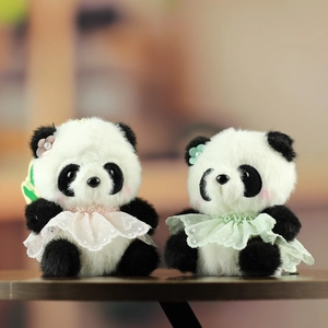 Dettaglio di portachiavi panda in peluche con gonne di pizzo rosa e verde su legno