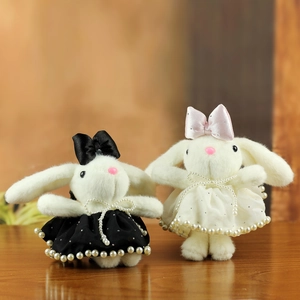 Cute bunny plush keychains with bowknots and pearl dresses on a wooden surface