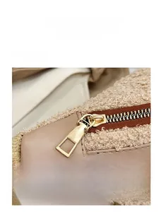 Detail of smooth golden metal zipper on cream plush teddy fabric and beige leather bag