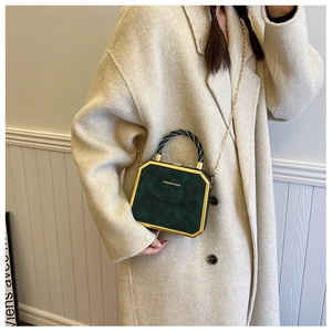 Detail of dark green octagonal crossbody bag with gold chain held by a model