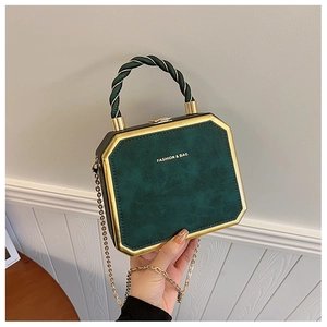 Groene en gouden harde handtas in detail, met elegante gedraaide handgreep en metalen ketting.